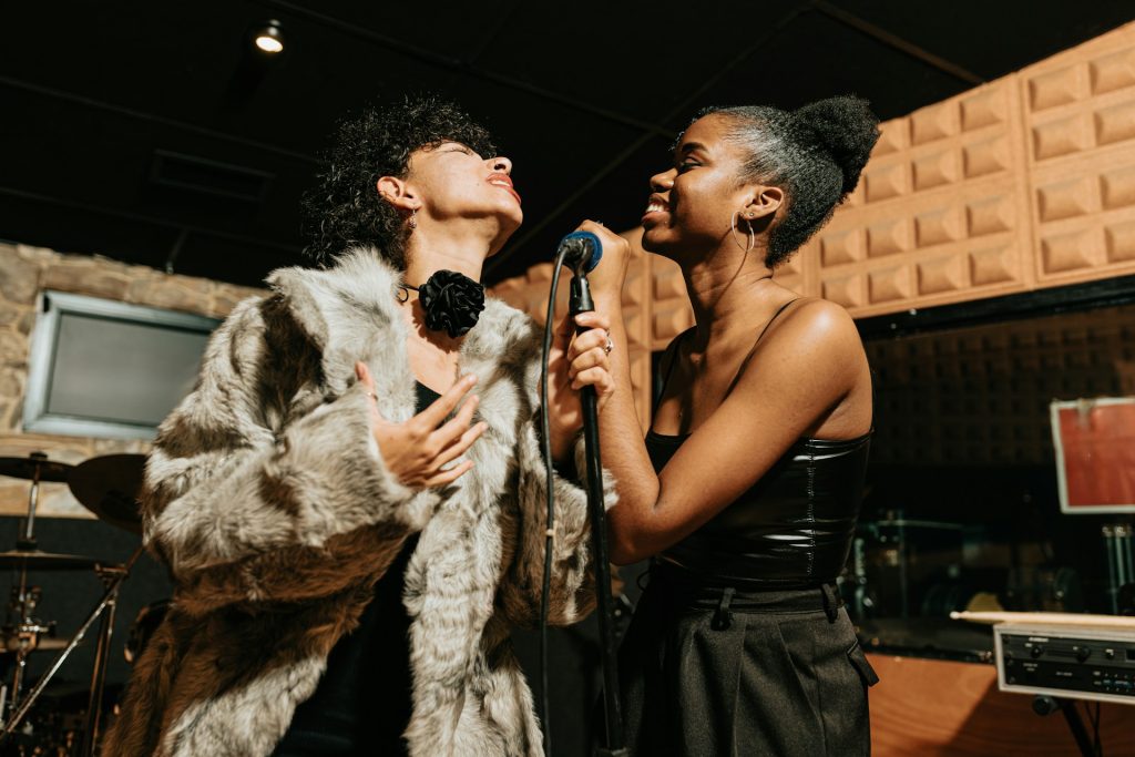 Deux chanteuses s'entraînent en souriant devant un micro.